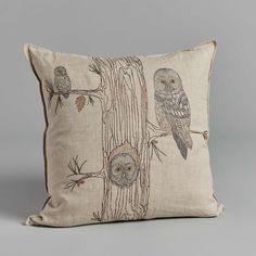 an embroidered pillow with owls and pine cones on the front, sitting on a tree branch