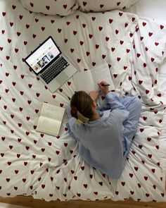 a woman laying in bed with two laptops and books next to her on the bed