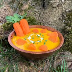 carrots are in a bowl on the ground next to a tree trunk and grass