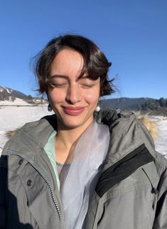 a woman is standing in the snow with her eyes closed and she's smiling