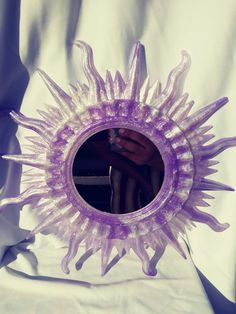 a purple sunburst shaped mirror sitting on top of a white sheet