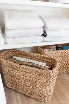 two baskets with towels on top of them in front of a shelf filled with folded towels