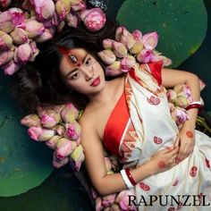 a woman in a white and red sari laying on top of water lillies