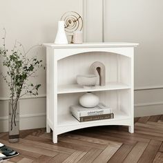 a white shelf with books and vases on it next to a phone, plant and other items