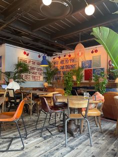 an empty restaurant with wooden tables and chairs, plants on the wall and posters on the walls