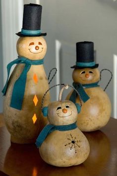 three wooden snowmen with hats and scarves on their heads, one wearing a top hat