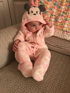 a baby sitting on a couch wearing a pink mickey mouse pajamas and a matching hat