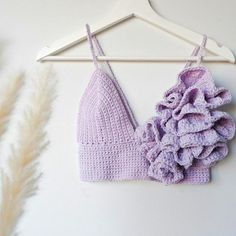 a crocheted bralet hanging on a hanger next to dried flowers and feathers