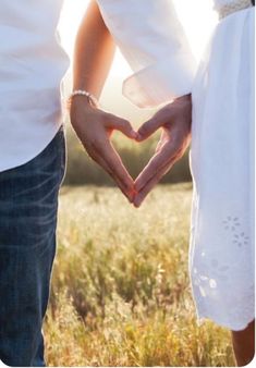 two people making a heart shape with their hands in the middle of them and grass behind them