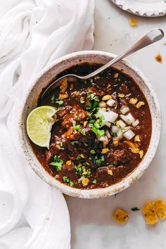 a person holding a spoon over a bowl of chili with corn and cilantro