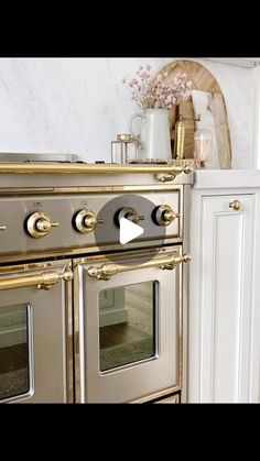 an old fashioned stove in a kitchen with white cabinets and gold trim on the doors