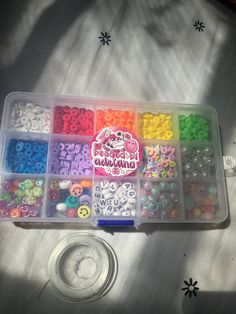 a plastic container filled with lots of different colored beads and buttons on a white surface