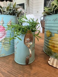 three tin canisters with plants and spoons in them sitting on a table