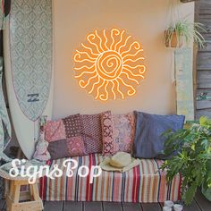 a neon sign that says sun above a couch with pillows and surfboards on it