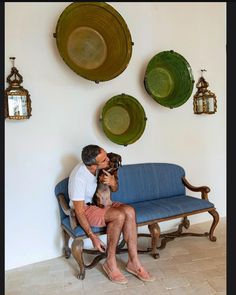 a man sitting on a blue couch with his dog in front of some plates hanging on the wall