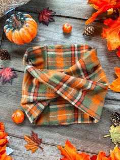 an orange plaid bow tie sitting on top of a wooden table surrounded by fall leaves