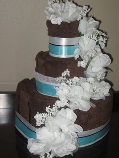 a three tiered cake with white flowers and blue ribbon on the top, sitting on a table