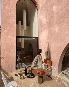 a woman sitting at a table with food and drinks in front of a pink building