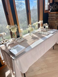 a table set up with white flowers and candles for an elegant wedding reception in front of a large window