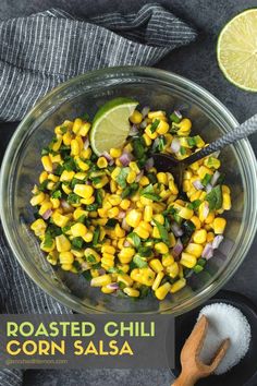 a glass bowl filled with corn and cilantro next to a lime wedge on a gray surface