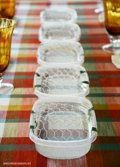 plastic containers lined up on top of a table covered in plaid cloth and glassware