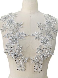 the back of a white dress with silver flowers and crystals on it's shoulders