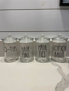 four glass jars with the words hair pins written on them are sitting on a counter