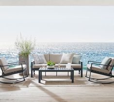 an outdoor seating area overlooking the ocean with chairs and tables on it's deck