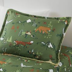 a bed covered in green and white sheets with forest animals on the pillowcases