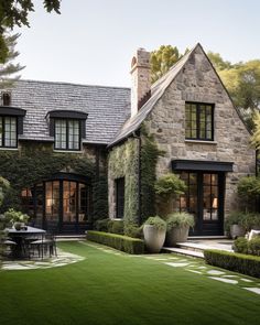 a stone house with black doors and windows in the front yard is surrounded by greenery