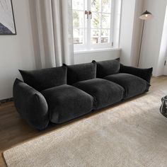 a black couch sitting on top of a wooden floor next to a white rug in front of a window