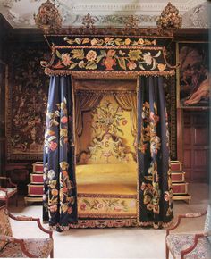 an elaborately decorated canopy bed in a room with chairs and paintings on the walls