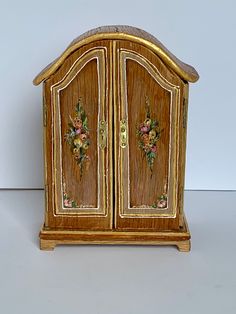 an ornate wooden cabinet with flowers painted on the front and sides, sitting on a white surface