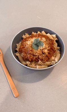 a bowl of pasta with meat sauce and parmesan cheese on top next to a wooden spoon