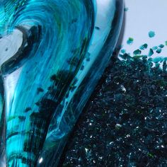 blue and green glass is sitting on the ground next to some black gravel with small pieces of seaweed in it