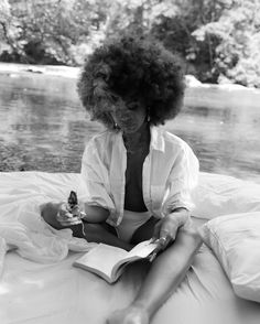 a black and white photo of a woman sitting on a bed with an open book