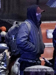 two people standing under an umbrella in the rain, one holding a teddy bear and wearing a face mask