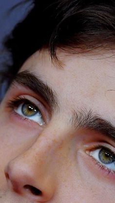 a close up of a man's face with brown hair and blue eyes looking at the camera