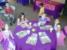 several children sitting around a purple table with plates and napkins on top of it