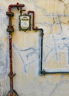 an old wall with pipes and a clock on it's side, next to a fire hydrant