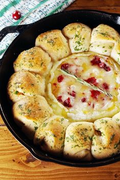 a skillet filled with bread and cheese on top of a wooden table next to a napkin