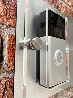 a ring video camera mounted to a brick wall next to a metal door handle on a stainless steel surface