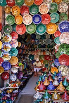 there are many colorful plates on display in the store, and one person is looking at them