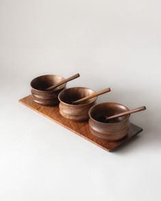 three wooden bowls with chopsticks in them on a wood tray against a white background