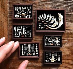 four wooden boxes with different designs in them on a wood table, one is holding a finger