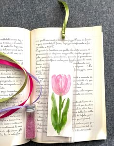 an open book with a watercolor painting of a pink tulip on it and ribbon