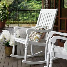 a white rocking chair sitting on top of a wooden deck next to a potted plant