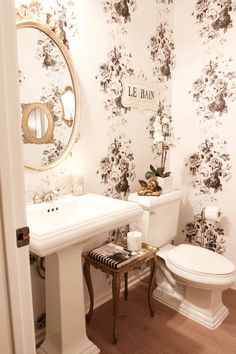 a white toilet sitting next to a sink in a bathroom under a mirror with black and white flowers on it