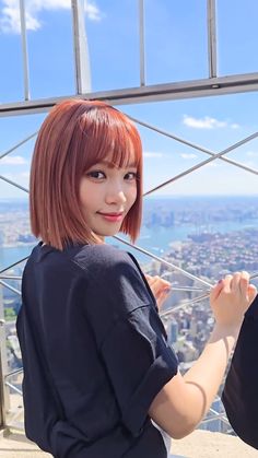 a woman with red hair sitting on top of a building looking at the camera and smiling