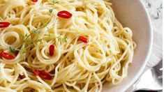 a white bowl filled with pasta and topped with red chili peppers next to a fork